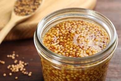 Photo of Whole grain mustard in jar on wooden table, closeup