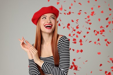 Photo of Young woman under heart shaped confetti on light grey background