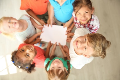 Photo of Little children holding sheet of paper in hands together indoors, top view. Unity concept