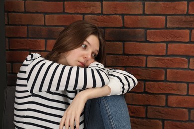 Sad young woman near brick wall, space for text