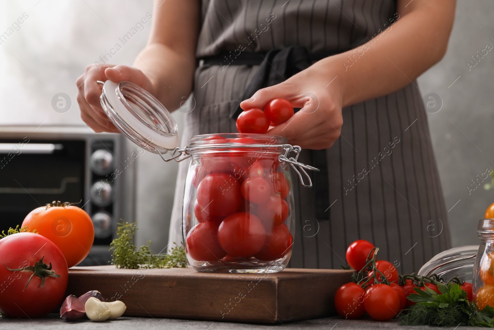 Photo of Woman putting tomatoes into glass jar at kitchen table, closeup. Pickling vegetables