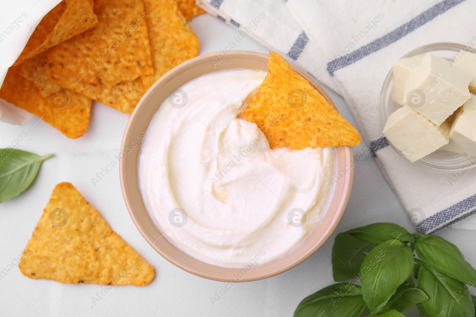 Photo of Delicious tofu sauce served with nachos chips on white tiled table, flat lay