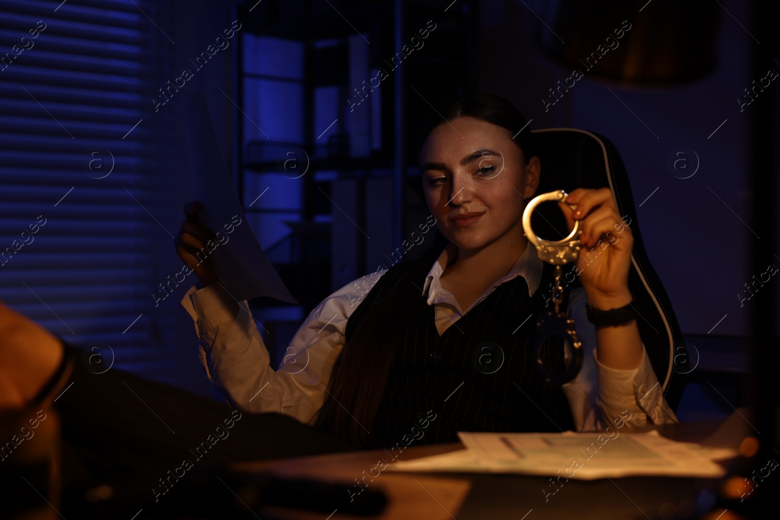 Photo of Professional detective with document and handcuffs at table in office at night