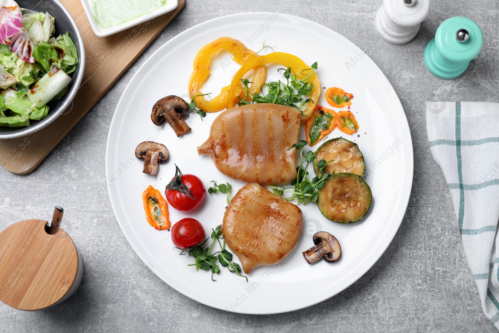 Photo of Delicious grilled squid tubes served on grey table, flat lay