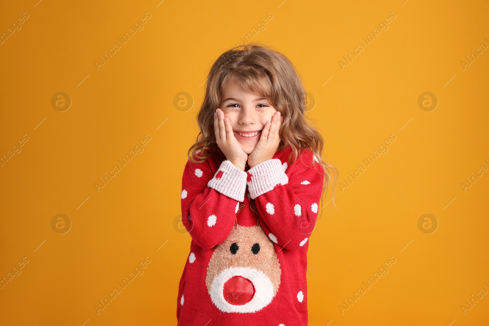 Photo of Cute little girl in red Christmas sweater smiling against orange background