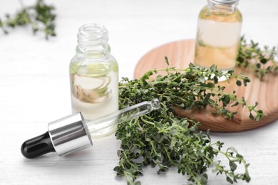 Photo of Thyme essential oil and fresh plant on white wooden table