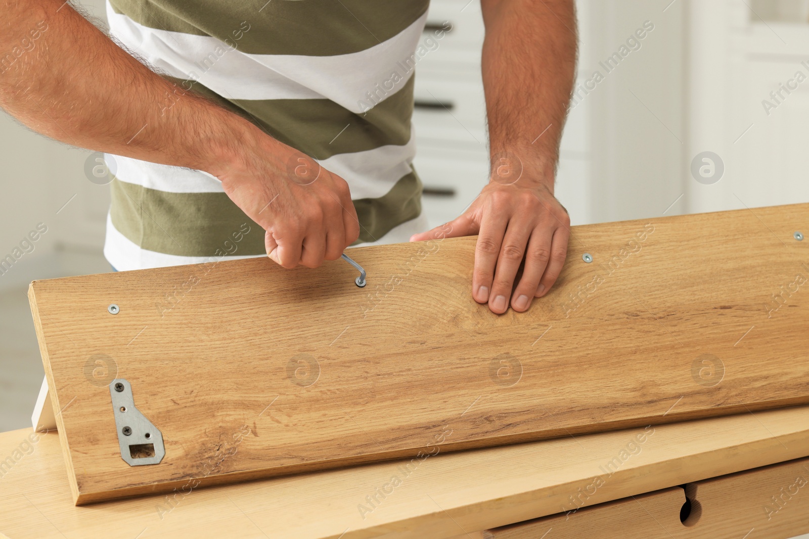 Photo of Man with hex key assembling furniture at table indoors, closeup