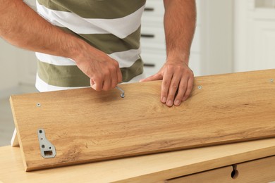Photo of Man with hex key assembling furniture at table indoors, closeup