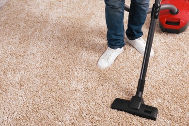 Man cleaning carpet with vacuum cleaner at home, closeup. Space for text