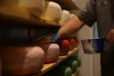 Photo of Worker coating cheese with wax in factory warehouse, closeup