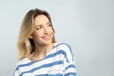 Portrait of happy young woman with beautiful blonde hair and charming smile on light background. Space for text