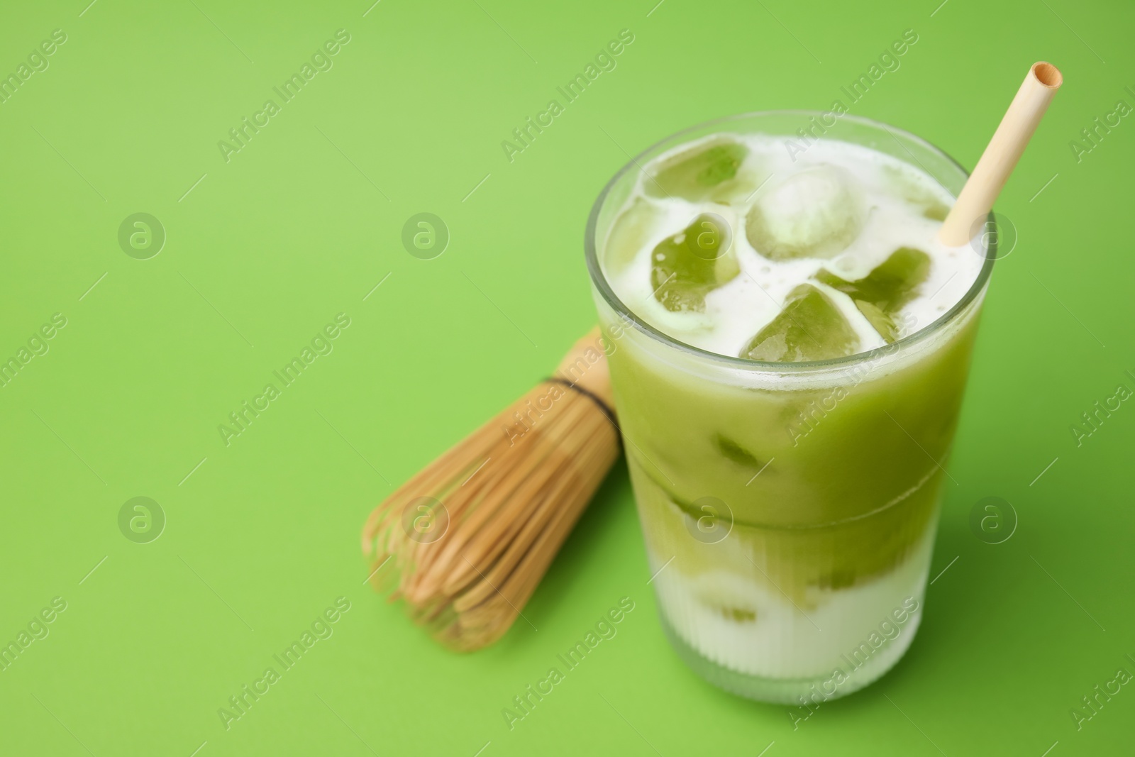 Photo of Glass of tasty iced matcha latte and bamboo whisk on light green background. Space for text