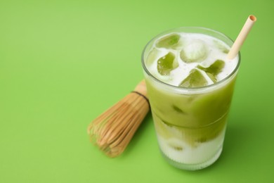 Photo of Glass of tasty iced matcha latte and bamboo whisk on light green background. Space for text