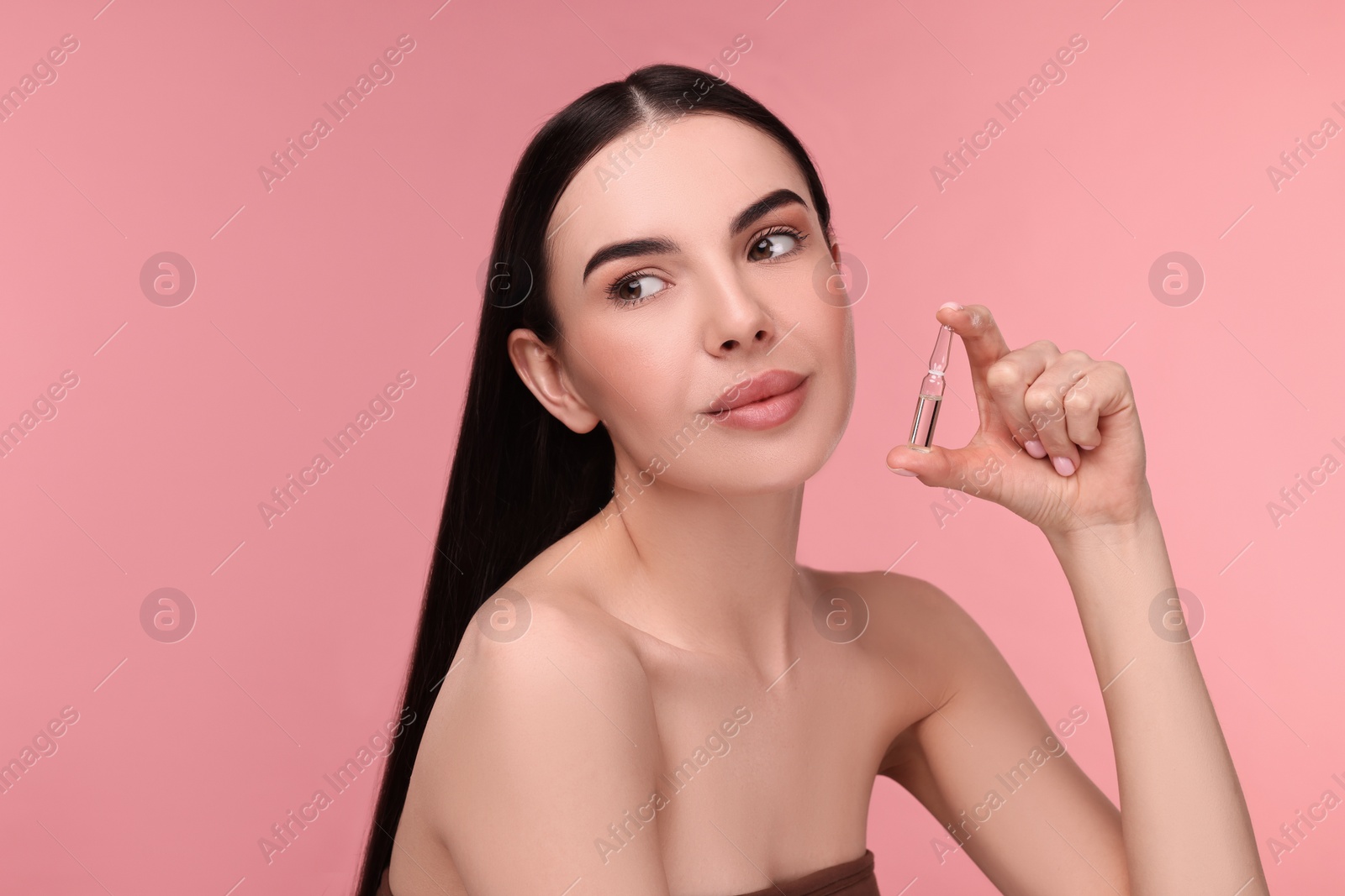 Photo of Beautiful young woman holding skincare ampoule on pink background