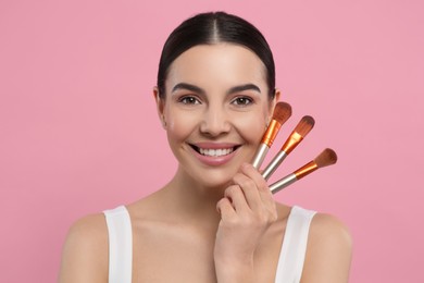 Photo of Happy woman with different makeup brushes on pink background