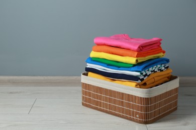 Photo of Laundry basket with clean stacked clothes on floor near grey wall. Space for text