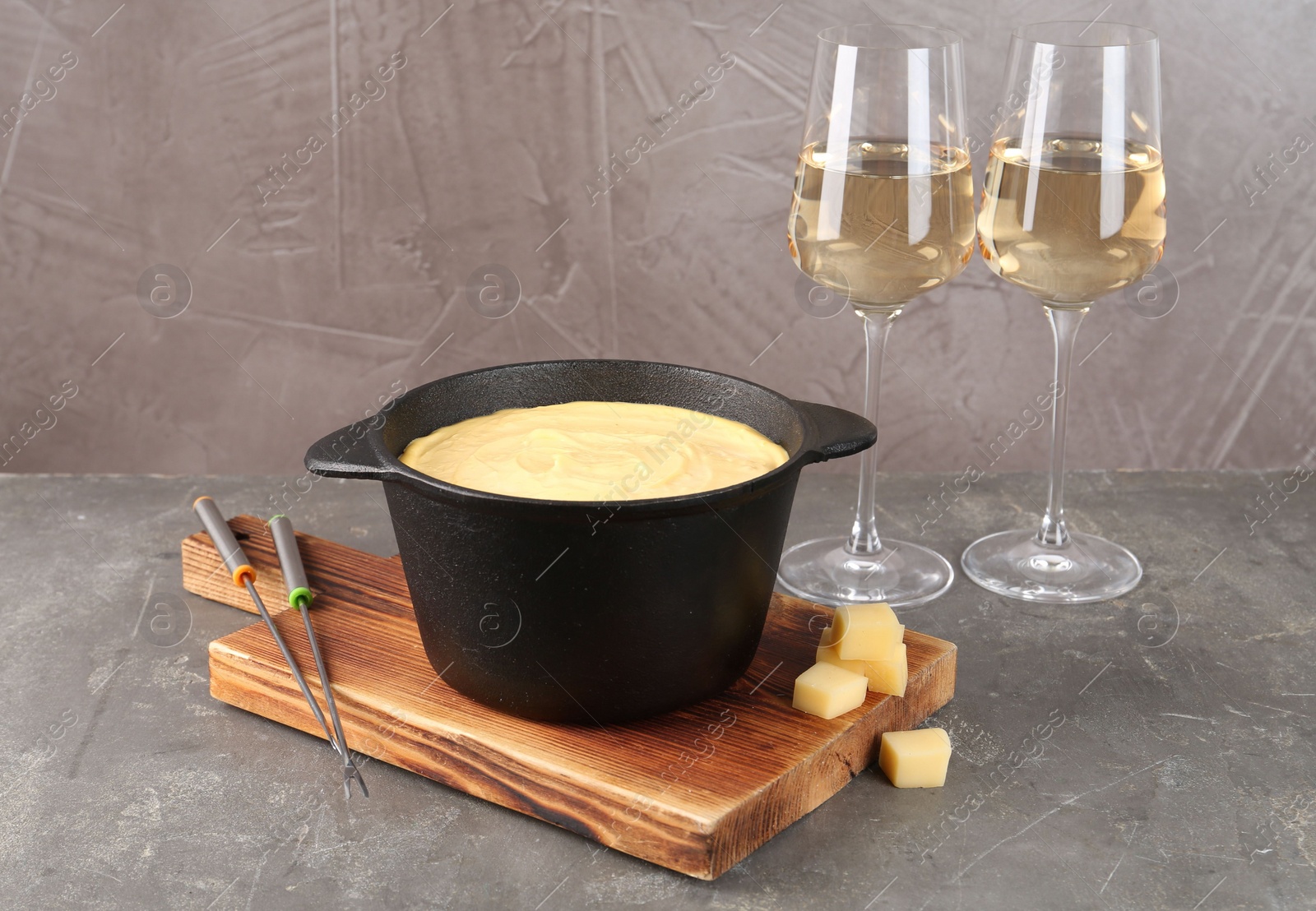 Photo of Fondue pot with tasty melted cheese, forks and wine on grey table