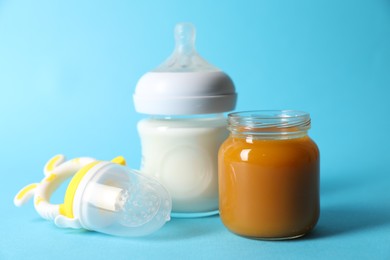 Photo of Jar with healthy baby food, bottle of milk and fruit feeder on light blue background