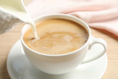 Photo of Pouring milk into cup of hot coffee on wooden table, closeup