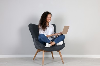 Photo of Young African-American woman working on laptop in armchair indoors