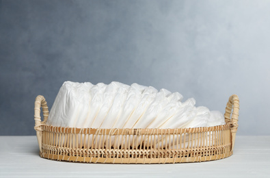 Photo of Tray with baby diapers on white wooden table against grey background