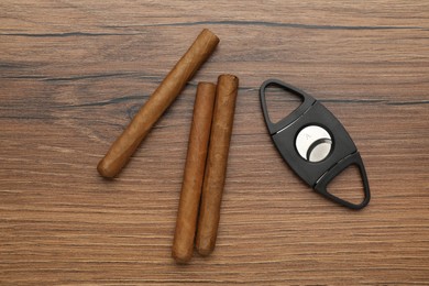 Photo of Cigars and guillotine cutter on wooden table, flat lay
