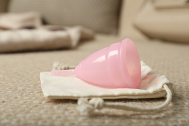 Photo of Pink menstrual cup with bag on sofa, closeup