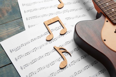 Photo of Guitar and sheets with music notes on wooden table