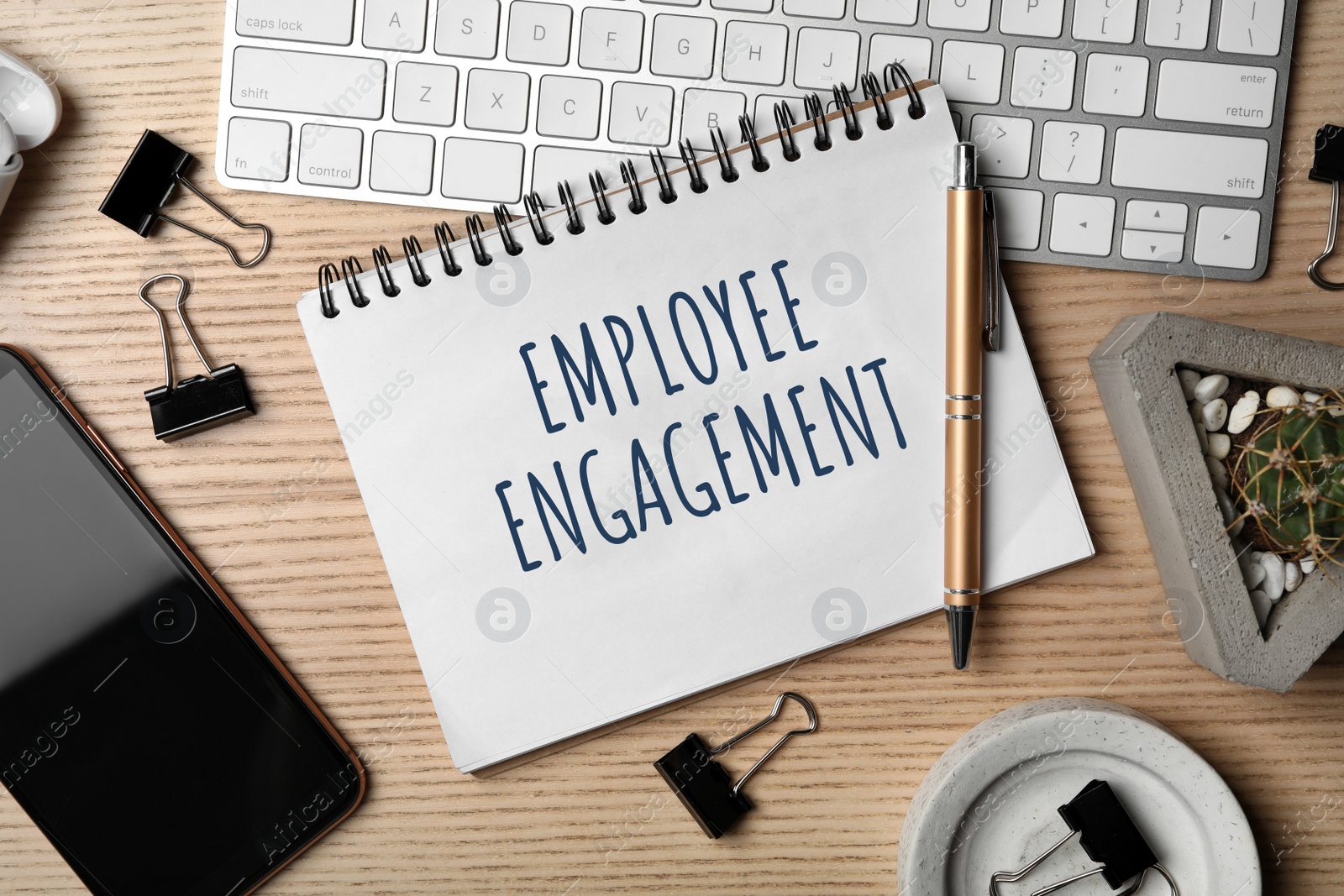 Image of Notebook with text EMPLOYEE ENGAGEMENT and stationery on wooden table, flat lay