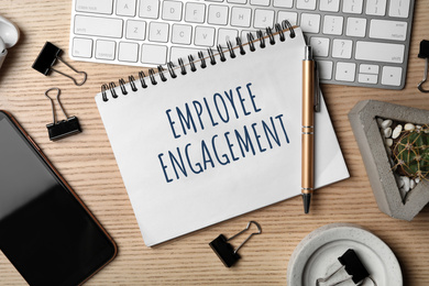 Image of Notebook with text EMPLOYEE ENGAGEMENT and stationery on wooden table, flat lay
