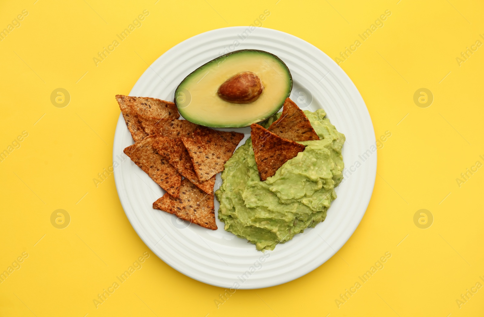 Photo of Delicious guacamole, avocado and nachos on yellow background, top view