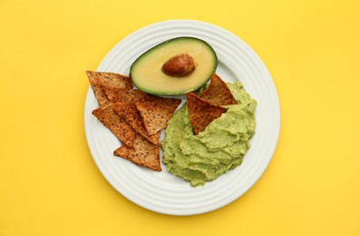 Photo of Delicious guacamole, avocado and nachos on yellow background, top view