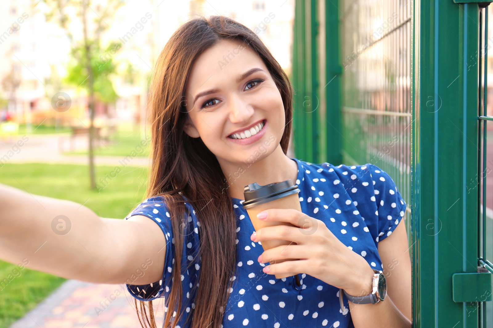 Photo of Young woman with cup of coffee taking selfie outdoors