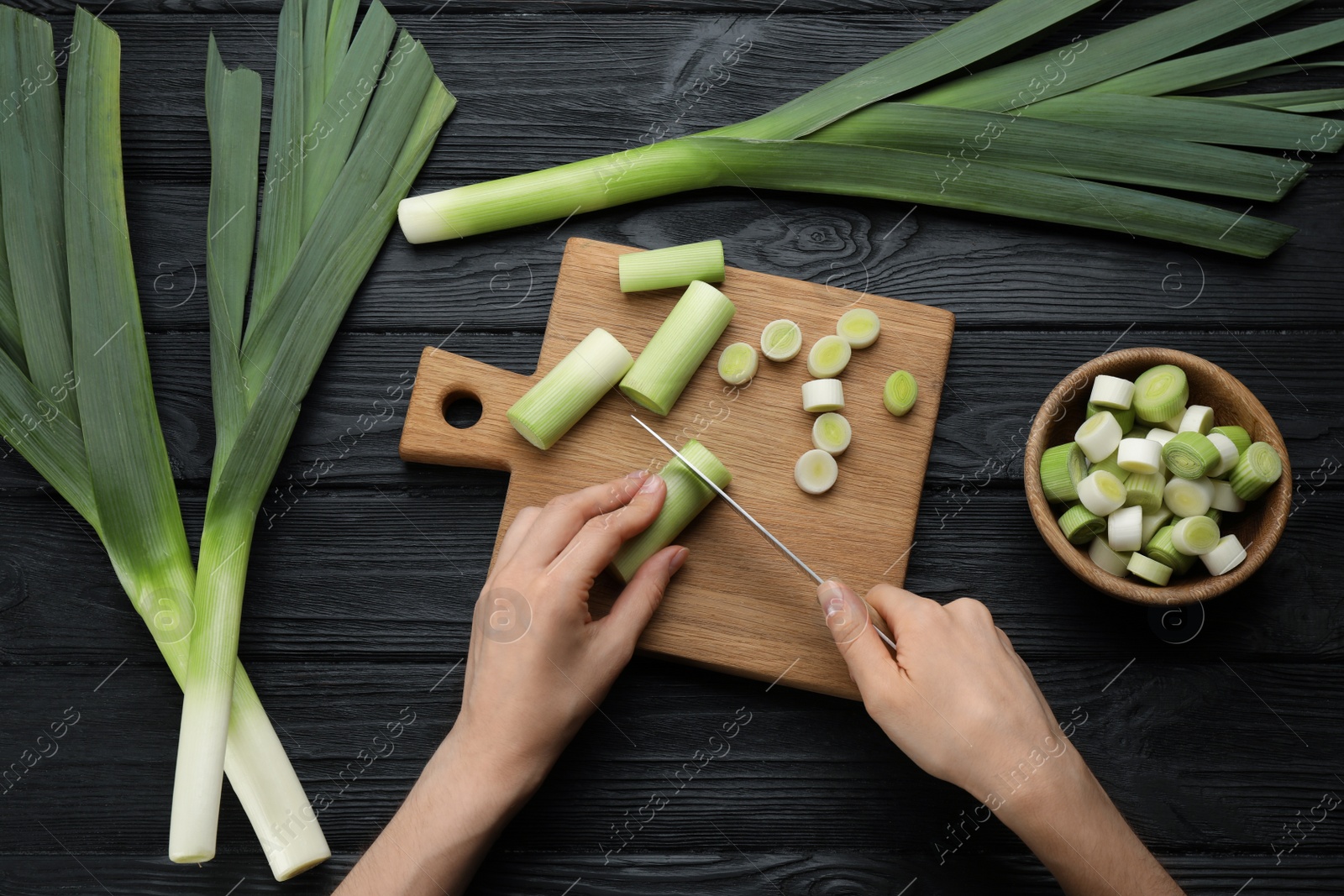 Photo of Woman cutting fresh raw leek at black wooden table, top view