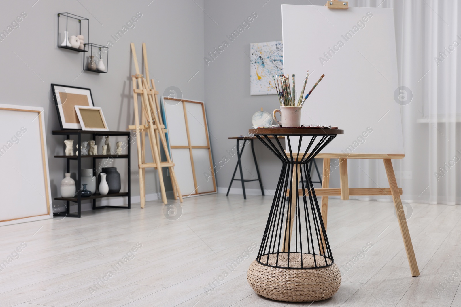 Photo of Wooden easel with canvas near paints and brushes in artist's studio, space for text