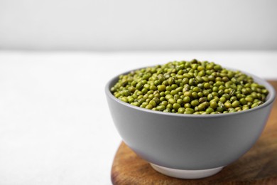 Photo of Bowl with green mung beans and wooden board on white table, closeup. Space for text