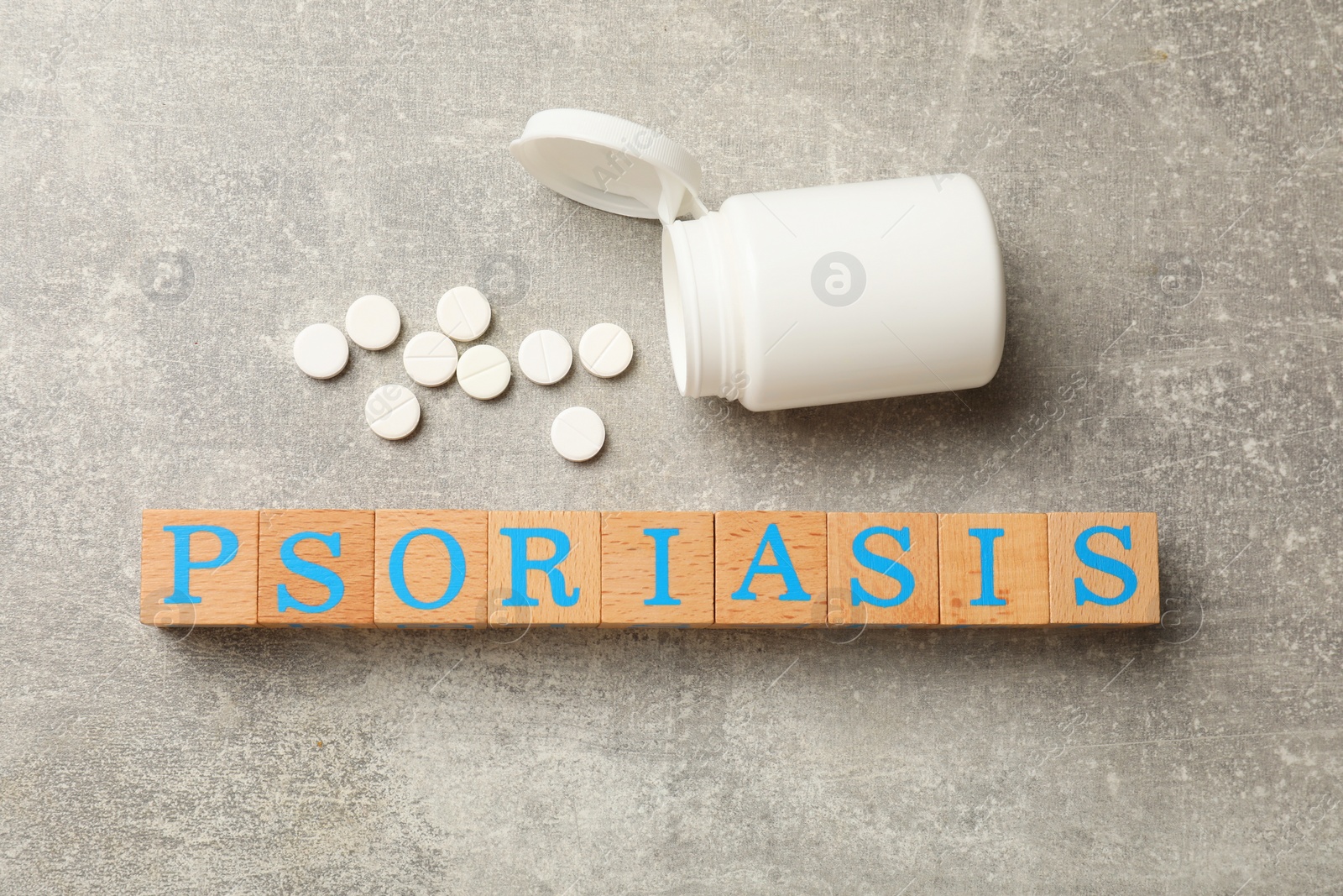 Photo of Word Psoriasis made of wooden cubes with letters and pills on light gray textured table, flat lay