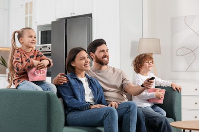 Photo of Happy family watching TV with popcorn on sofa at home