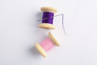 Photo of Colorful sewing threads with needle on white background, top view