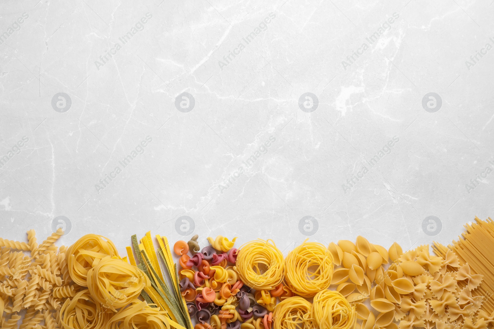 Photo of Different types of pasta on light grey marble table, flat lay. Space for text