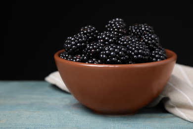 Fresh ripe blackberries in bowl on blue wooden table against dark background, closeup