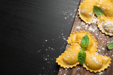 Raw ravioli with basil on black wooden table, flat lay and space for text. Italian pasta