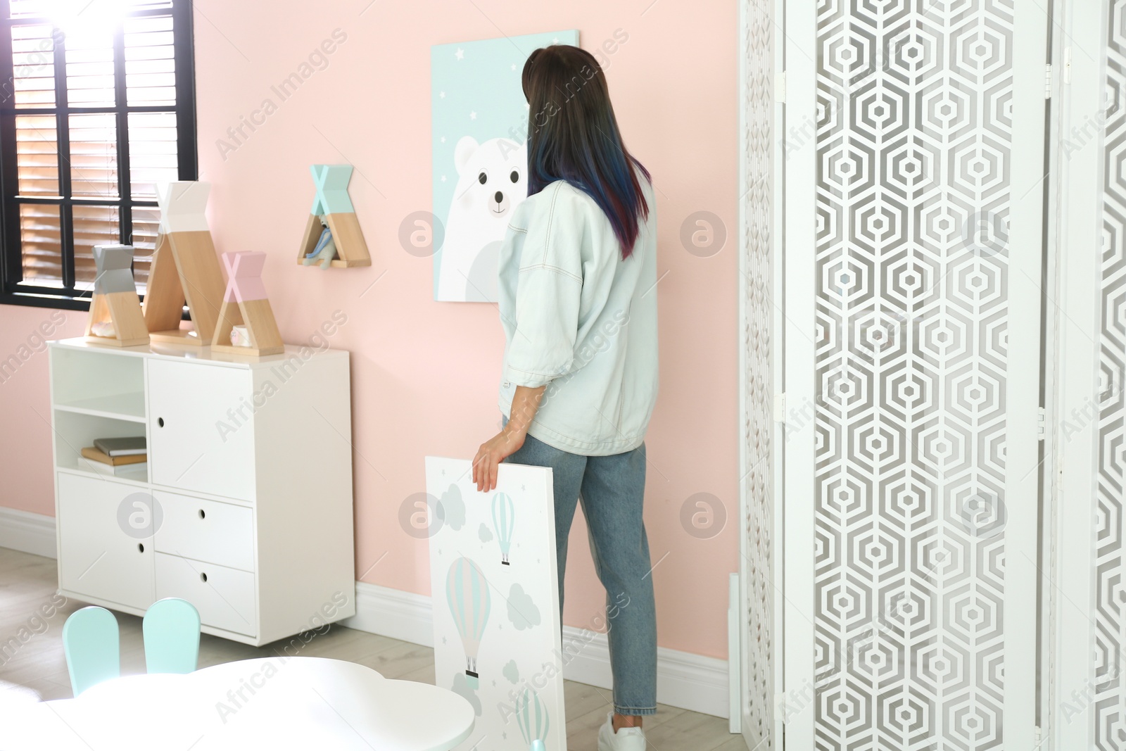 Photo of Decorator hanging pictures on pink wall. Children's room interior design