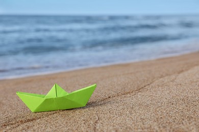 Light green paper boat near sea on sandy beach, space for text