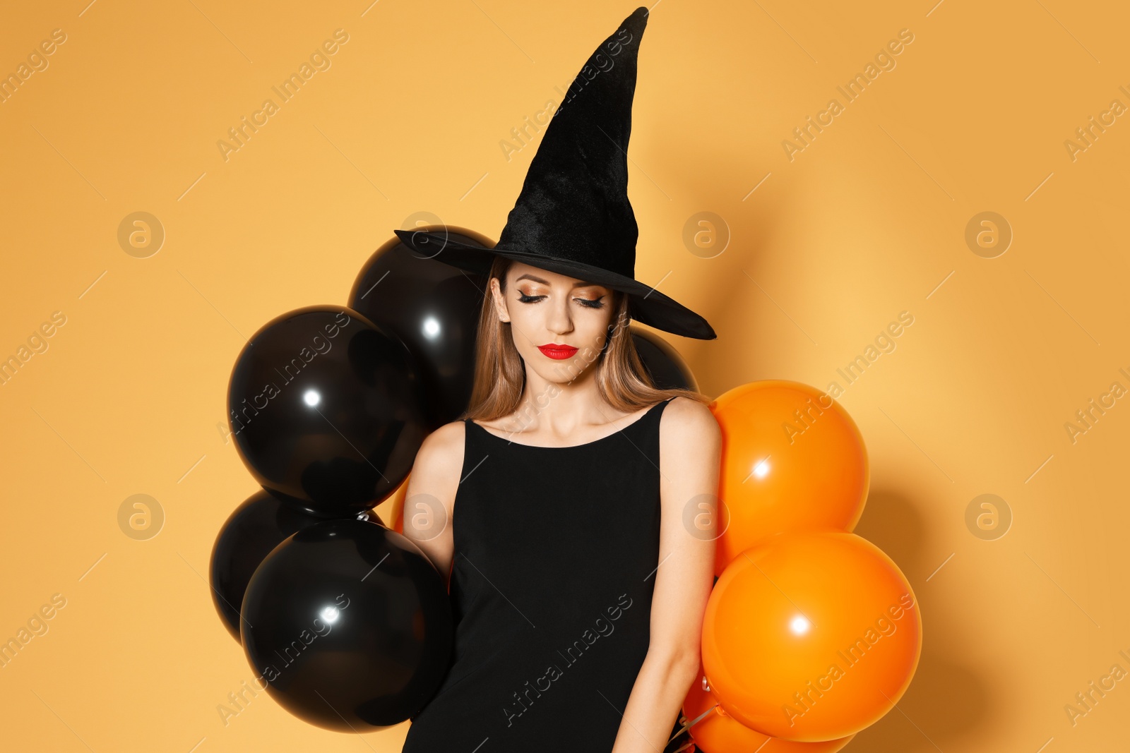 Photo of Beautiful woman wearing witch costume with balloons for Halloween party on yellow background