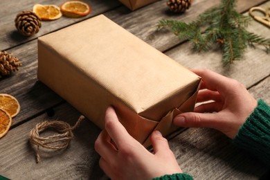 Christmas present. Woman wrapping gift box with kraft paper at wooden table, closeup