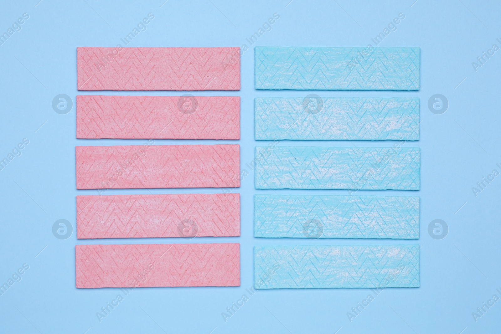 Photo of Sticks of tasty chewing gum on light blue background, flat lay