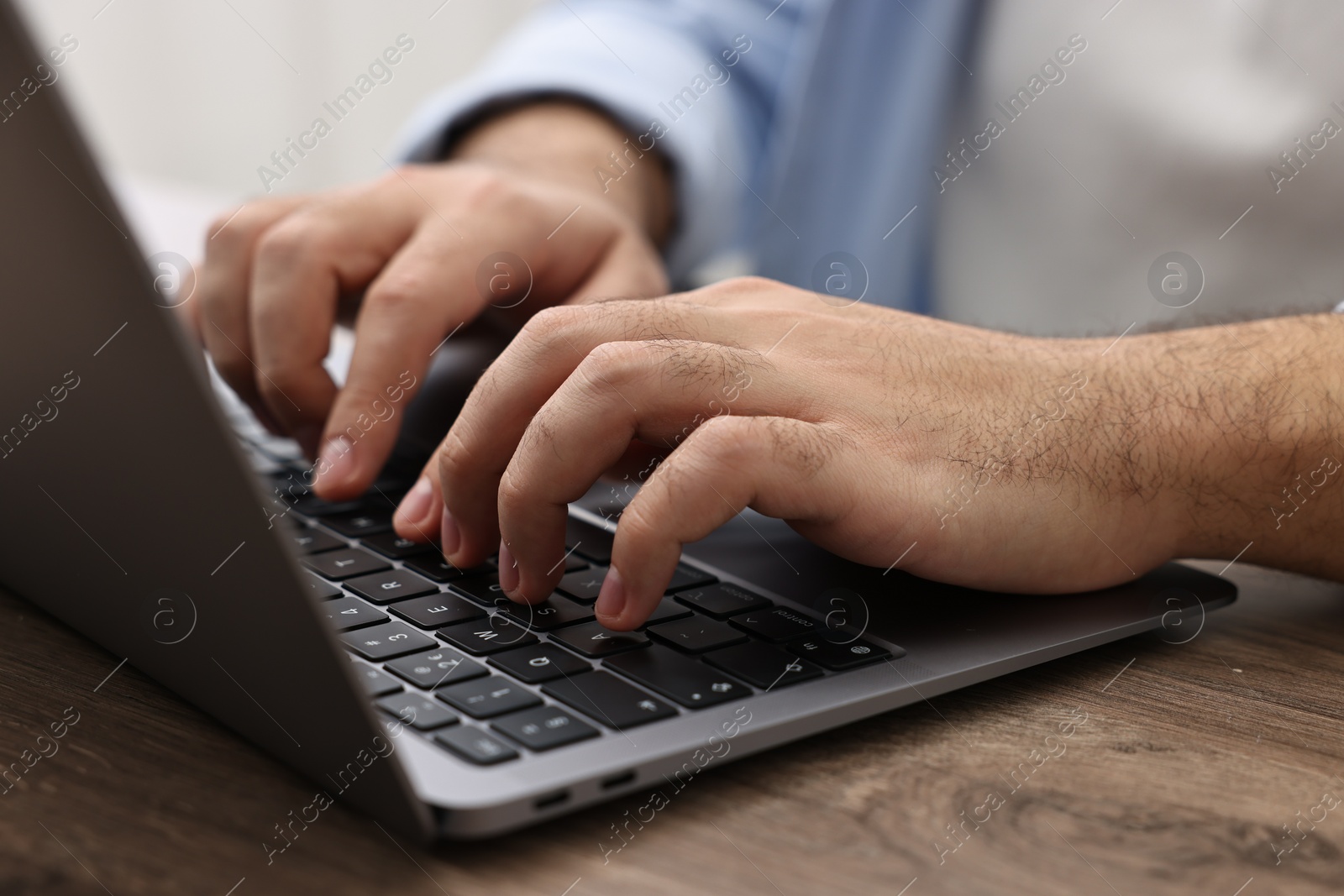 Photo of E-learning. Young man using laptop at wooden table, closeup