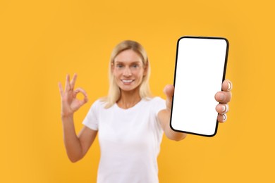 Photo of Happy woman holding smartphone with blank screen and showing OK gesture on orange background, selective focus