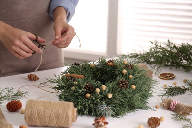 Photo of Florist making beautiful Christmas wreath at white wooden table indoors, closeup